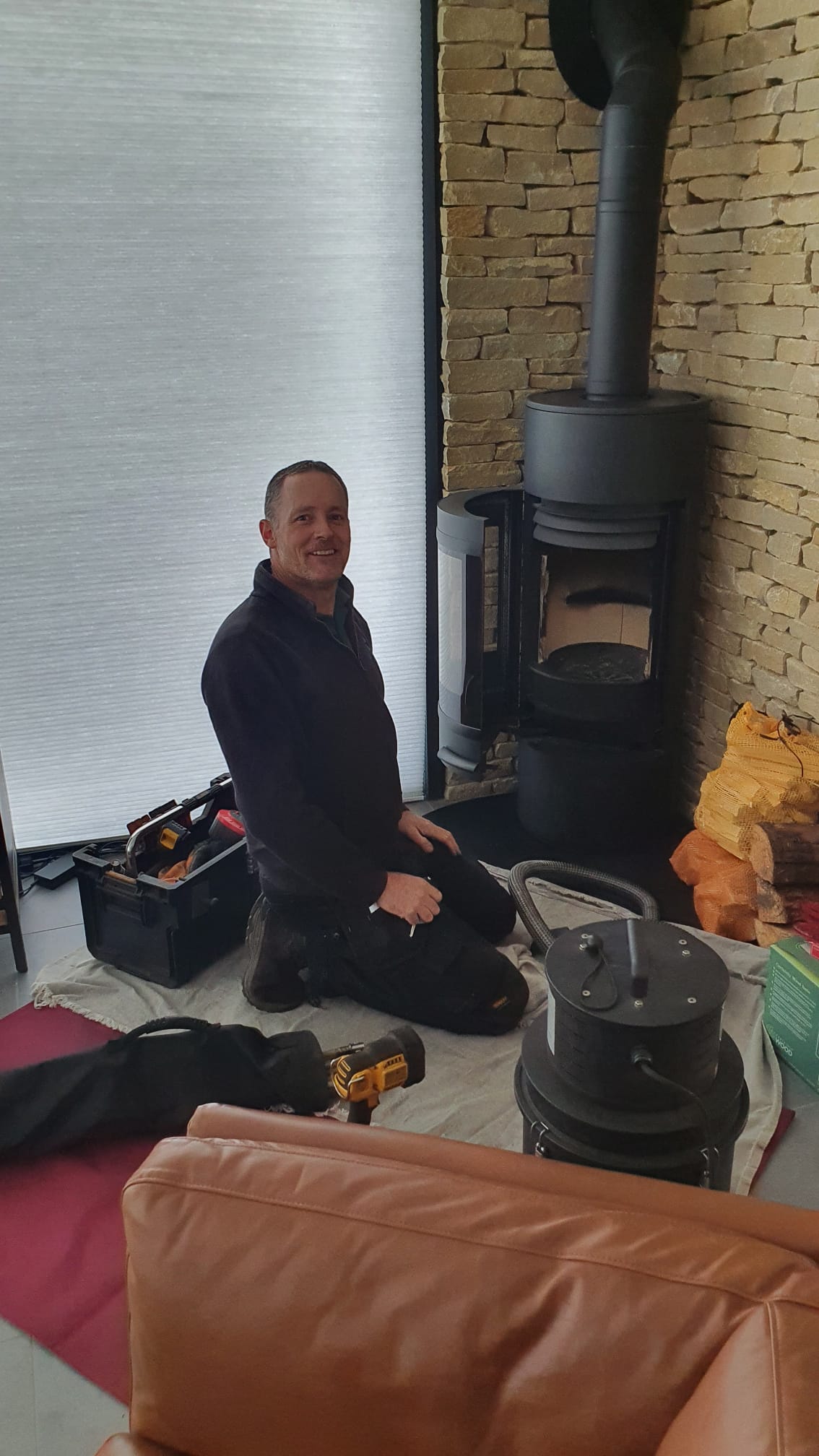 Mayn Stubley kneeling on a dust sheet beside a woodburner he is sweeping